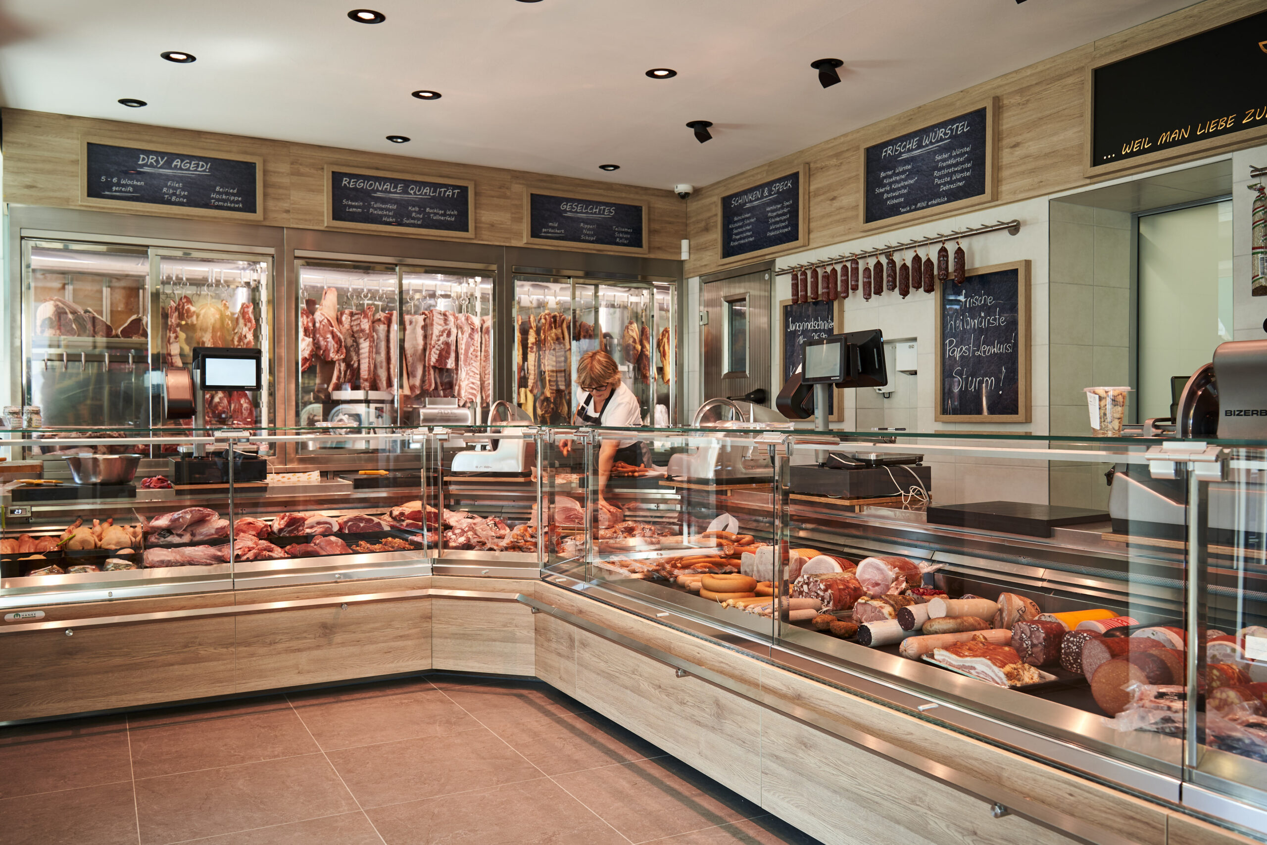 Ein Ort, an dem Handwerk sichtbar wird: Die neue Theke der Fleischerei Hödl ist mehr als nur Verkaufsfläche – sie ist Bühne, Schaufenster und Statement zugleich. Auf über sieben Metern entfaltet sich ein Panorama regionaler Fleischkultur, präsentiert mit Liebe zum Detail in einem modernen Ladenbaukonzept.